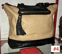 Front view of beige and black leather soft-sided handbag with black leather tassel and zip pocket, showing base and handles.