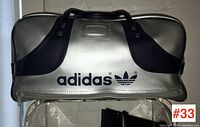 Front view of the vintage Adidas silver sports bag with black handles and Adidas branding.