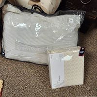 Photo showing two Calvin Klein pillows and one Calvin Klein sheet set, all packaged in clear plastic, lying on carpeted floor.