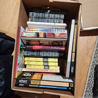 Photo of a box filled with assorted books including legal guides, cookbooks, fiction, and reference books, some with visible titles and varying binding styles.