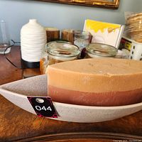 Candles in assorted shapes and colors on a wooden surface including a large triangular three-wick candle resting on a white patterned ceramic tray.