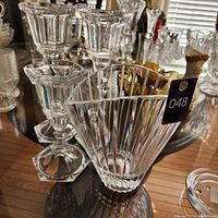 Photo showing four clear crystal pieces on a wooden surface: one fluted vase and three intricately designed candle holders with faceted detailing.