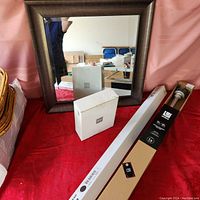 Framed mirror, Mikasa picture frame box, Ikea wall hook strip box, Umbra drapery rod box displayed on red surface