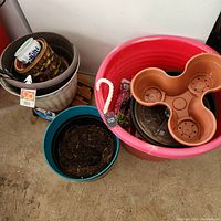 Overview of flower pots including a large red plastic tub, blue pot with soil, three-section beige saucer tray, and a nested set of pots inside a large gray pot.
