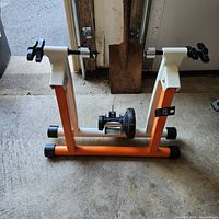 Side angle photo of the orange and white magnetic indoor bike trainer stand on concrete floor.