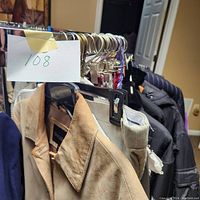 Photo showing beige/tan men's jacket, black quilted jacket, and pants on hangers