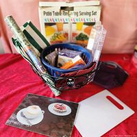 Photo showing black wire basket with rolled cotton napkins, utensils and packages, white cutting board, serving tray, and boxed Patio Table Revolving Serving Set.