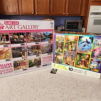 Photo of two Sure-Lox Art Gallery deluxe puzzle sets on countertop. Boxes show puzzle images, piece counts and feature sealed puzzle pieces inside.