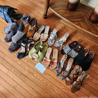 Photo showing an assortment of 13 gently used women's shoes arranged on hardwood floor, including various styles such as boots, heels, sandals, and slippers.