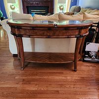 Full view of sofa table showing wood finish, curved legs, glass inset top, and lower shelf.