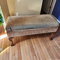 Full view of the rectangular upholstered storage bench showing fabric wear and carved wooden legs.