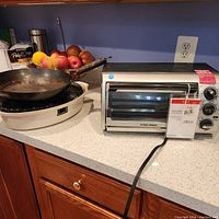 Black & Decker toaster oven sitting next to electric circular grill with removable wok pan on a kitchen counter.