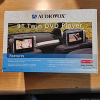Boxed Audiovox 9" Twin DVD Player set with feature summary.