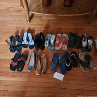 Overview of 12 pairs of assorted women's shoes laid on wooden floor showing different styles and colors.