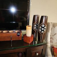 Photo of the set of 4 wooden candle holders on a glass top cabinet with a TV and chair nearby.
