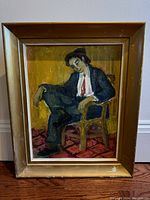 Front view of oil painting by Wahdi el Mahdy showing a seated man in a dark suit seated on a wooden chair over a red patterned rug against a yellow background in a gilt wood frame with visible scuffs.