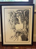 Framed black and white print showing a seated angel with curly hair and detailed wings.