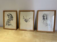 Photo showing three framed untitled sketches leaning against a wall. Images depict bird on rocks, bird in flight, and a portrait of a person with a head covering.