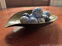 View of leaf-shaped plastic bowl holding nine decorative blue and white porcelain balls on wooden floor