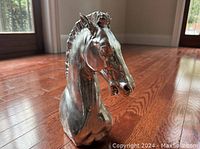 Left angled close-up of horse head sculpture showing facial details and smooth metallic finish on wooden floor.