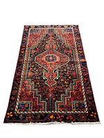 Full view of the Persian Nahavand rug laid out flat showing its geometric central motif and surrounding surreal plant and animal patterns in rich colors.