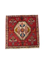 Full view of red Shiraz nomadic rug with central cream medallion and colorful geometric and animal motifs, diamond patterned border and fringes.