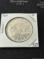Reverse side of 1960 Canadian 1 Dollar coin showing Voyageur and Indigenous person in canoe with date and denomination.