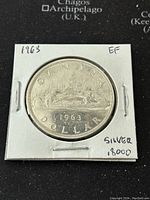 Reverse side of 1963 Canadian silver dollar coin showing canoe and date "1963" with "CANADA DOLLAR" inscription.