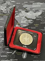 Photo of the silver commemorative coin in its presentation case on a map background.