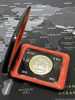 Coin inside closed black presentation case with red velvet lining showing dates 1873 and 1973 and inscriptions RCMP and GRC.
