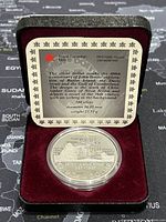 Open display case showing silver proof dollar coin and informational plaque inside the lid describing the coin and its history.