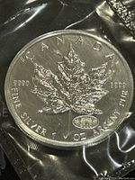 Obverse side of the coin showing the detailed maple leaf, purity markings, and the millennium privy mark on sealed packaging.