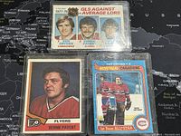 Three NHL goalie trading cards shown front side; Ken Dryden and Bernie Parent cards, in protective sleeves on black background with world map.