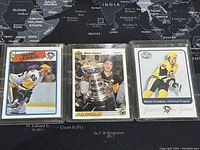 Front side of three Mario Lemieux trading cards displayed on a map background, showing Lemieux in a Pittsburgh Penguins uniform, one card with the Stanley Cup, and a 'Greats of the Game' card.