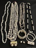 Full assortment of pearl necklaces, bracelets, and earrings laid out on black fabric showing variety of sizes and styles.