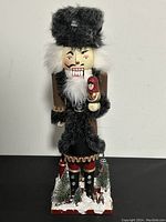 Front view of the nutcracker figurine showing detailed face, beard, hat, and doll held in hand.