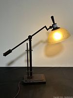 Front view of the large metal table lamp with lit frosted glass shade on black surface.