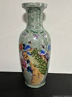Full view of the large oriental ceramic vase showing peacock and floral design on greenish-grey background.
