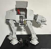 Large Star Wars AT-AT Walker with open side hatch showing 3 figures inside, 2 figures standing outside at the walker's feet on black surface.