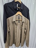 Two men's Lululemon button-up shirts hanging on hangers, one black and one beige.