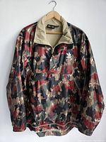 Full front view of the Adidas camouflage hoodie jacket hung on a wooden hanger against white background.
