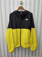 Front view of black and yellow The North Face windbreaker jacket on hanger