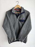 Full view of Patagonia Synchilla gray fleece pullover hung on a wooden hanger, showing quarter snap front and chest pocket.