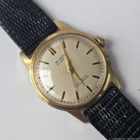 Front view of watch dial showing cream dial with gold-tone baton indices, “MIMO 25 Jewels Automatic Waterproof” branding, and black leather strap