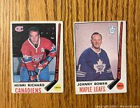 Front of two 1969-70 O-Pee-Chee hockey cards showing Henri Richard in a Canadiens uniform and Johnny Bower in a Maple Leafs uniform. Both cards have a hockey stick graphic and team logos.