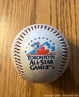 White baseball with colorful 1991 Toronto Blue Jays All-Star Game logo featuring maple leaf and baseball.