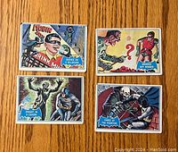 Four Batman cards laid out on wooden surface showing colorful comic-style illustrations with Robin and Batman in dynamic scenes.