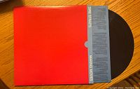 Vinyl record partially removed from red and blue sleeve showing front of album cover with band and album name.