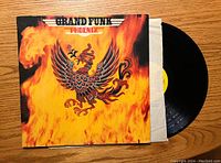 Front view of 'Phoenix' album cover featuring a fiery phoenix on flames background, with partially removed vinyl in sleeve.