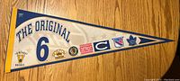 Front side of the Original 6 NHL felt pennant showing bright blue and white color with logos of Boston Bruins, Detroit Red Wings, New York Rangers, Toronto Maple Leafs, Chicago Blackhawks, and Montreal Canadiens along with vintage typography.